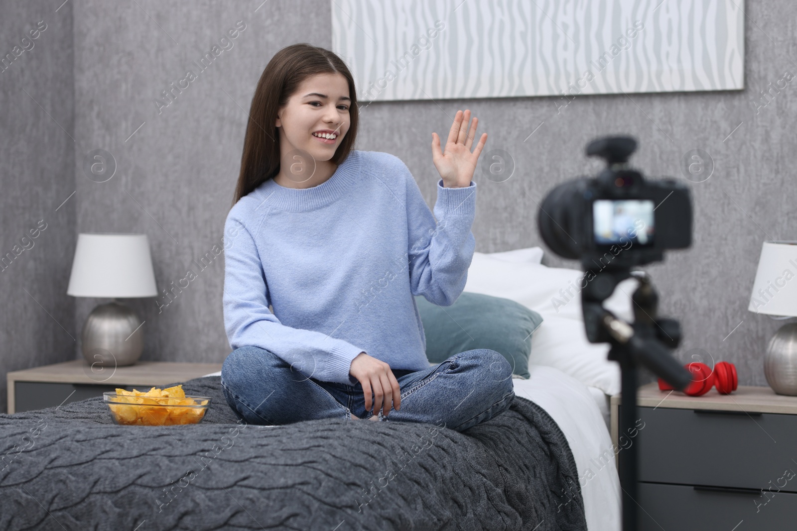 Photo of Smiling teenage blogger waving hello to her subscribers while streaming at home