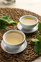 Photo of Green tea in white cups with leaves and wicker mat on table