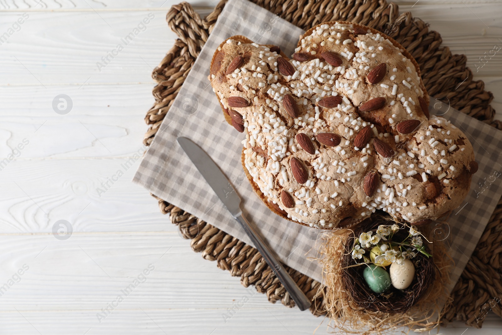 Photo of Delicious Italian Easter dove cake (Colomba di Pasqua) and decorative eggs on white wooden table, top view. Space for text