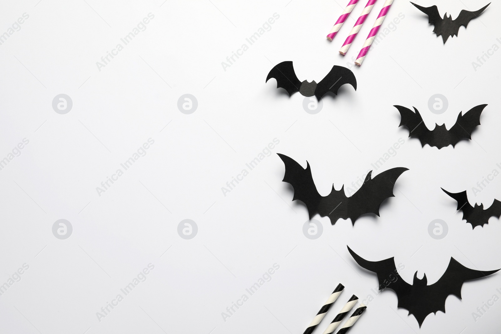 Photo of Flat lay composition with paper bats and straws on white background, space for text. Halloween celebration