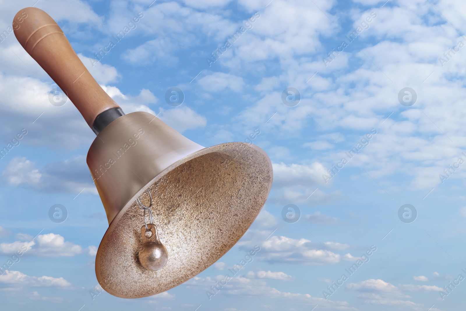 Image of Shiny school bell with wooden handle against blue sky