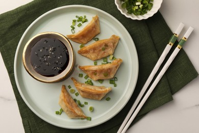 Photo of Delicious gyoza (asian dumplings) with soy sauce, green onions and chopsticks on white table, top view