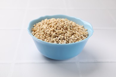 Photo of Dry pearl barley in bowl on white tiled table, closeup