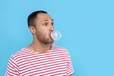 Photo of Young man blowing bubble gum on light blue background. Space for text