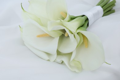 Beautiful calla lily flowers tied with ribbon on white fabric, closeup