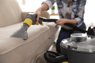 Photo of Woman removing dirt from sofa with vacuum cleaner at home, closeup