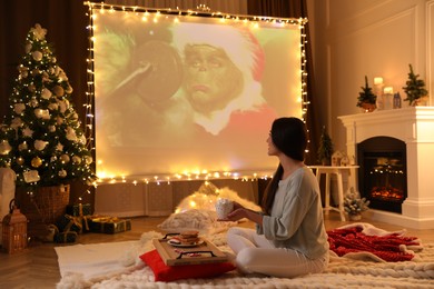 Photo of MYKOLAIV, UKRAINE - DECEMBER 24, 2020: Woman watching The Grinch movie via video projector in room. Cozy winter holidays atmosphere
