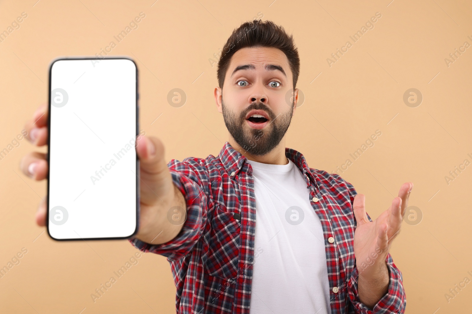 Photo of Surprised man showing smartphone in hand on beige background