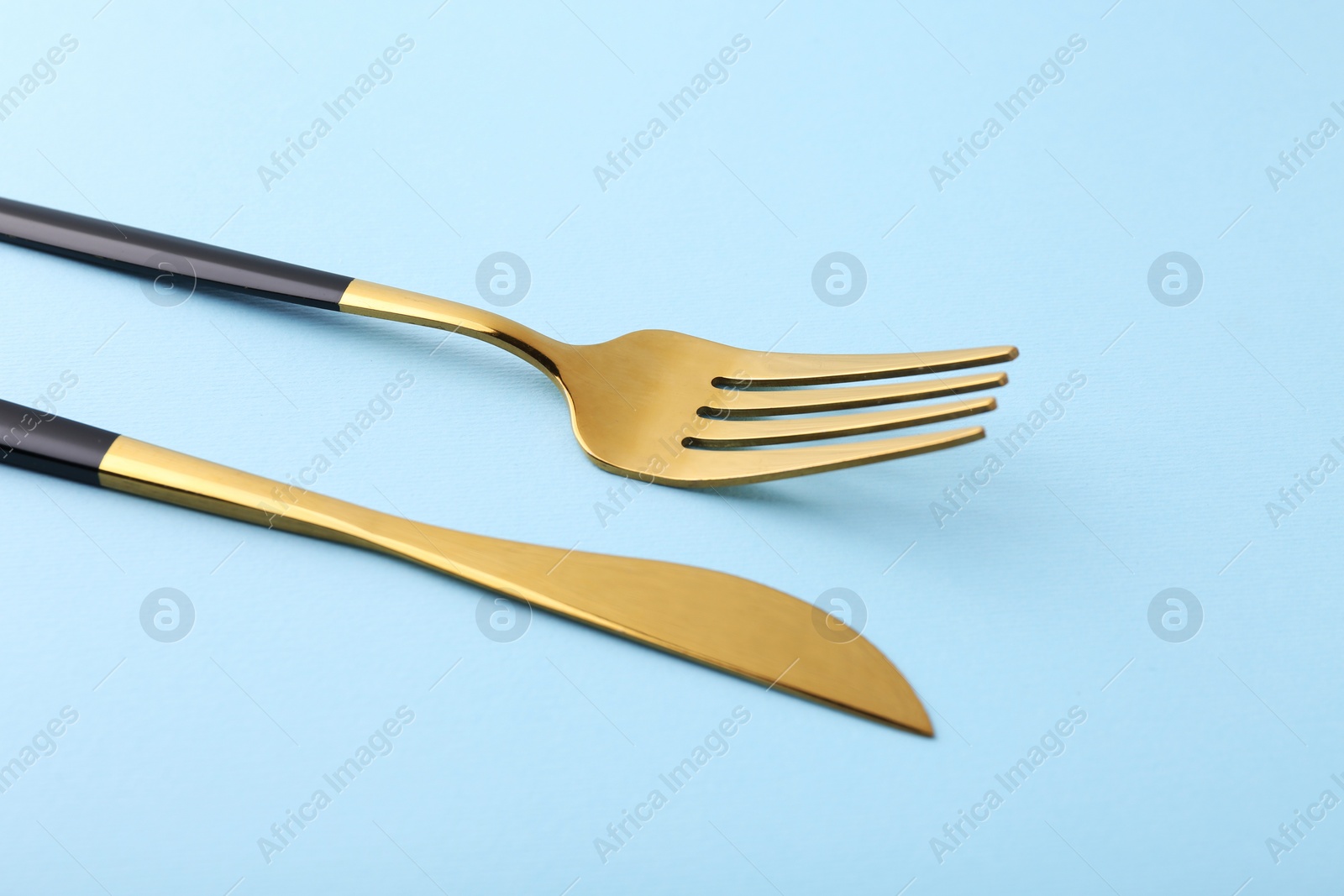 Photo of Stylish cutlery. Golden knife and fork on light blue background, closeup