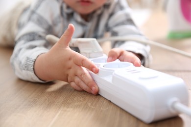 Photo of Little child playing with power strip and plug on floor indoors, closeup. Dangerous situation