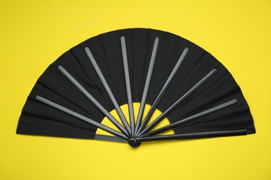 Photo of Stylish black hand fan on yellow background, top view