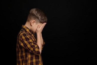 Boy covering face with hands on black background, space for text. Children's bullying