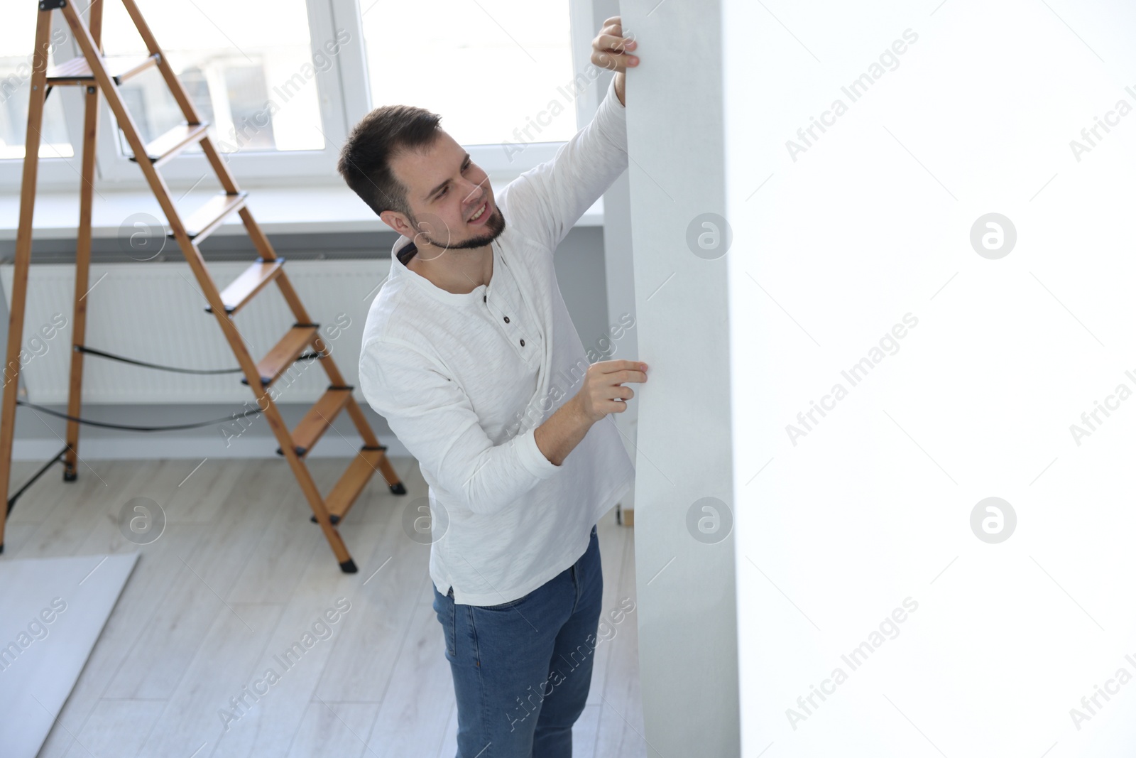 Photo of Man hanging stylish gray wallpaper in room