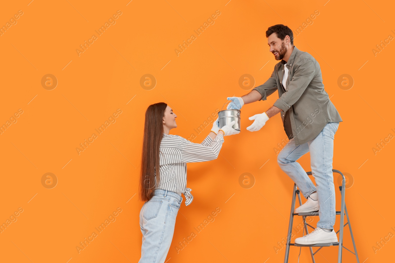 Photo of Woman giving man can of paint near orange wall. Interior design