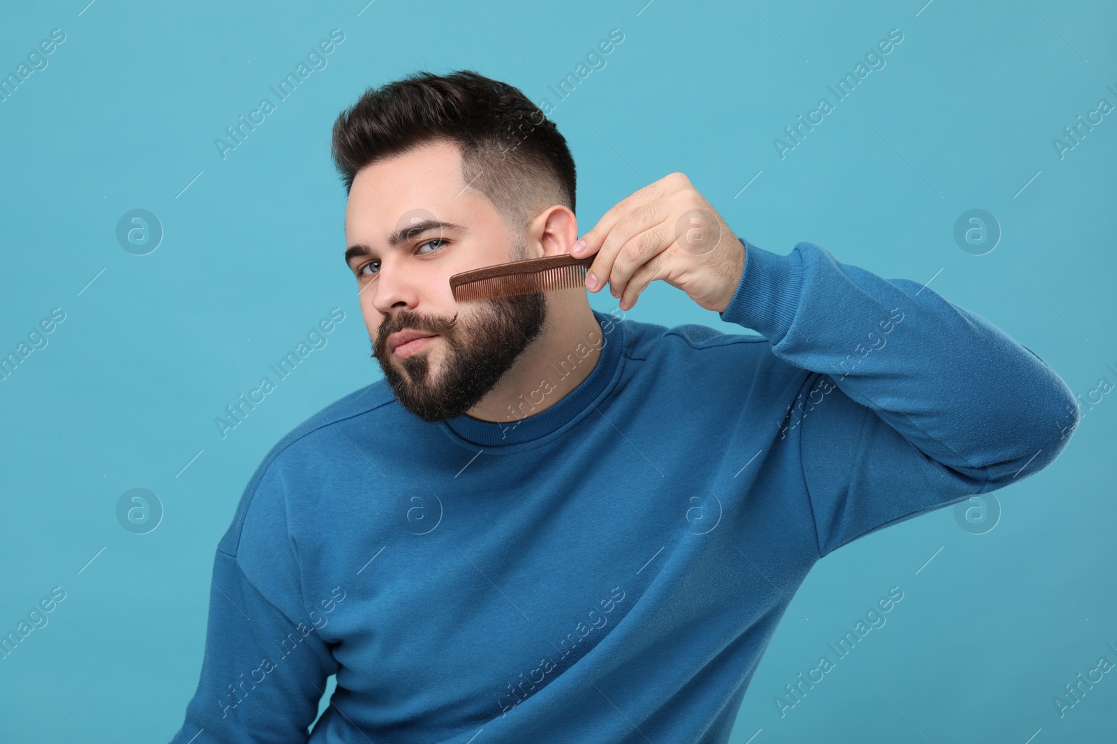 Photo of Handsome young man combing beard on light blue background