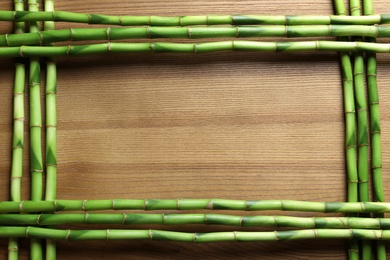 Photo of Green bamboo stems and space for text on wooden background, top view