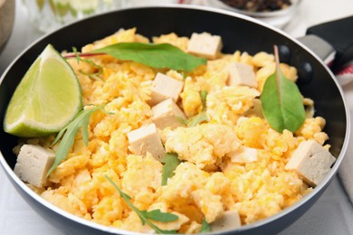 Photo of Frying pan with delicious scrambled eggs, tofu and lime on white table, closeup