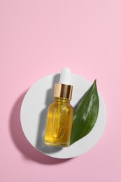Bottle of cosmetic oil and green leaf on pink background, top view