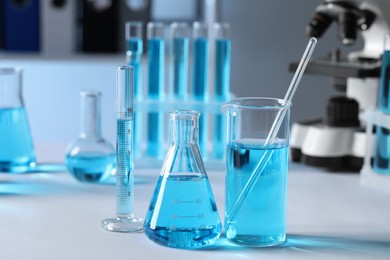 Different laboratory glassware with light blue liquid on table