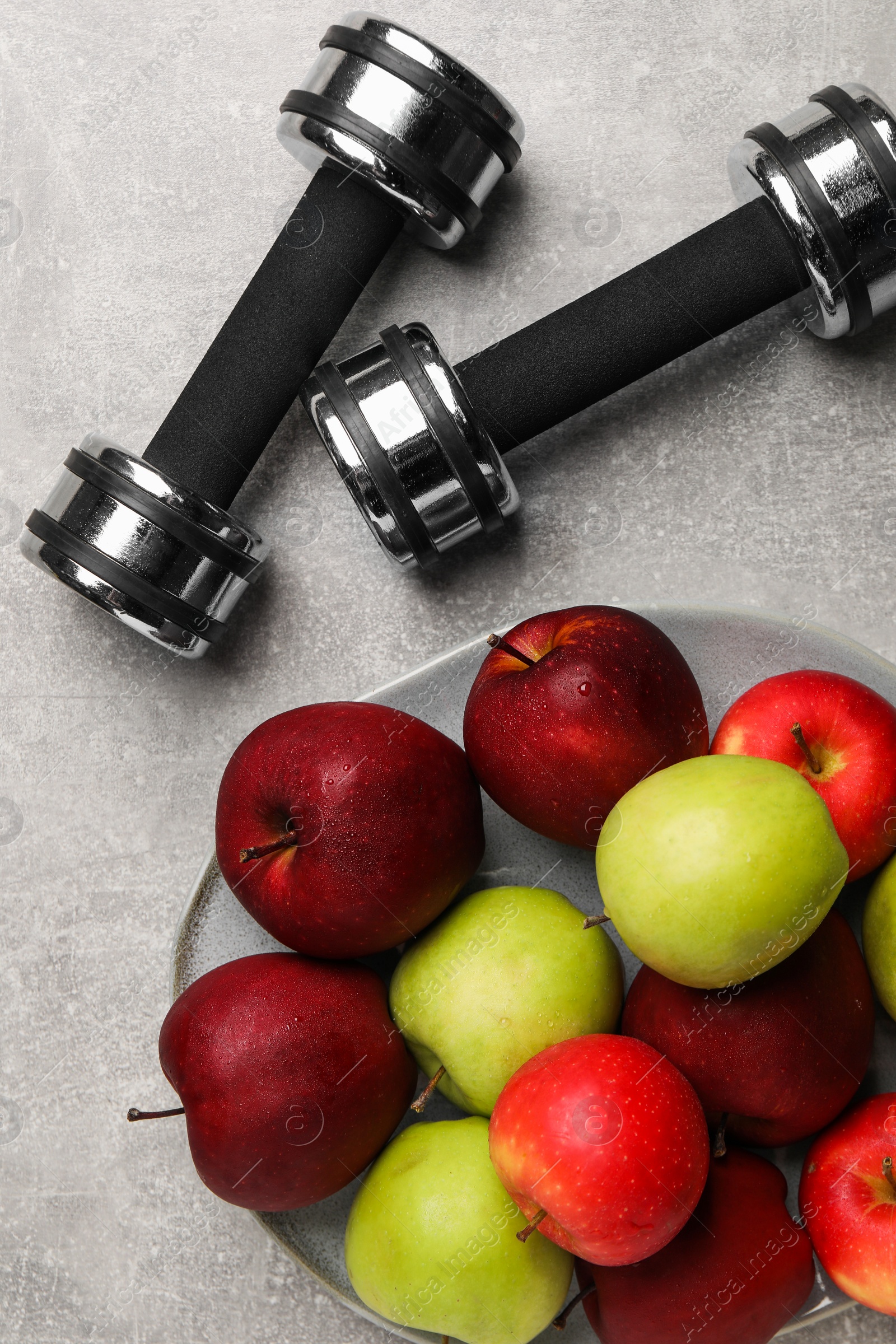 Photo of Healthy diet. Plate with apples and dumbbells on light grey textured table, flat lay