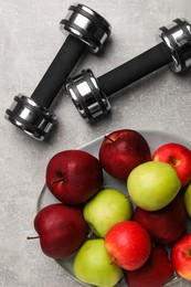 Healthy diet. Plate with apples and dumbbells on light grey textured table, flat lay