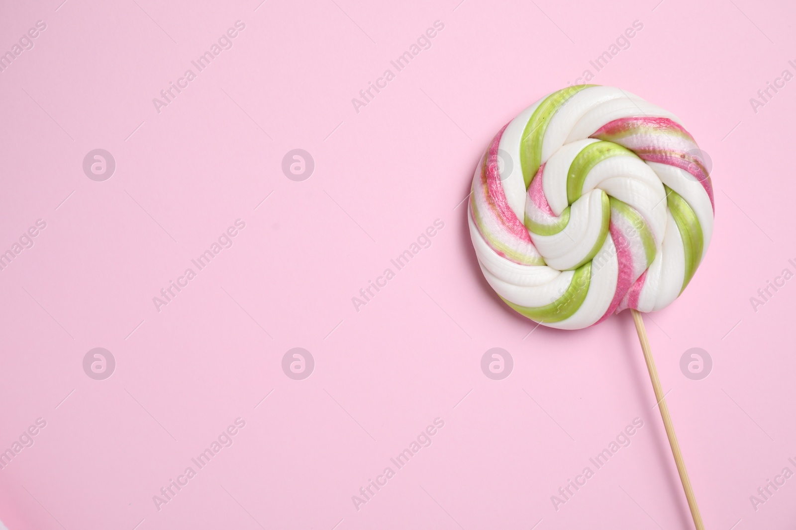 Photo of Stick with colorful lollipop swirl on pink background, top view. Space for text