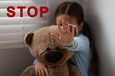 Image of No child abuse. Little girl with teddy bear making stop gesture indoors, selective focus