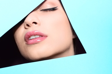 View of beautiful young woman with perfect lips makeup through cutout in color paper