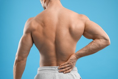 Man suffering from back pain on light blue background, closeup