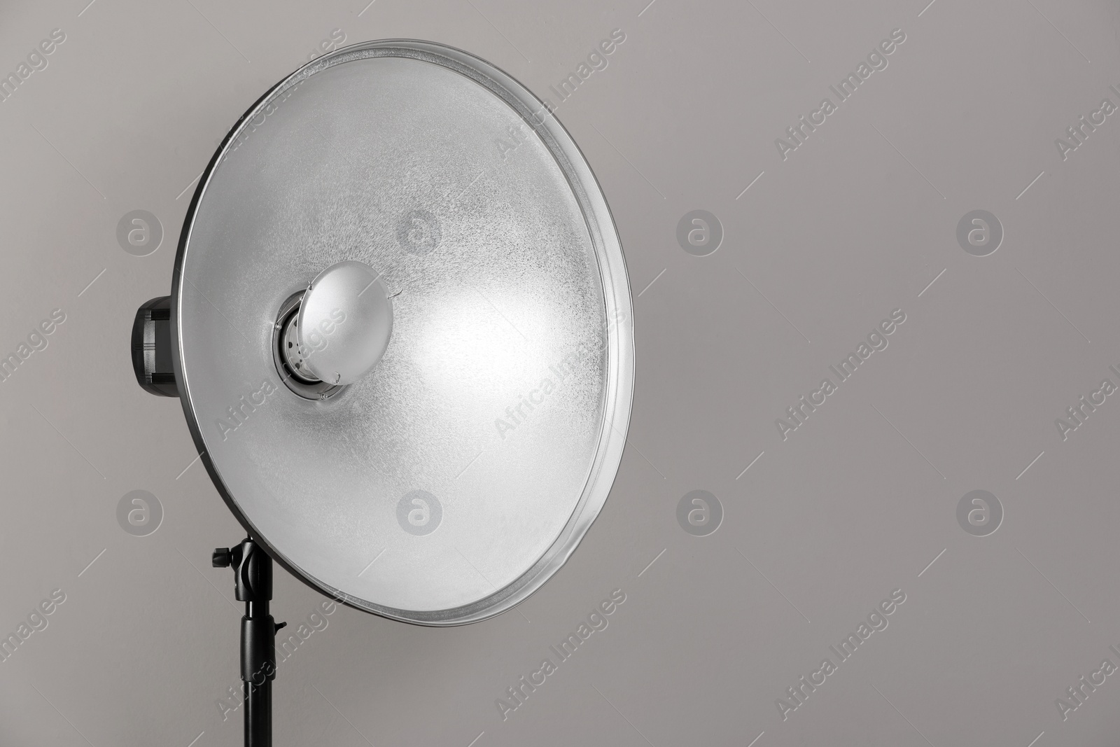 Photo of Professional beauty dish reflector on tripod against grey background, space for text. Photography equipment