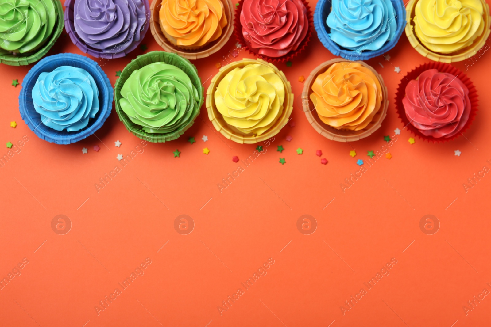 Photo of Delicious bright cupcakes and sprinkles on coral background, flat lay. Space for text