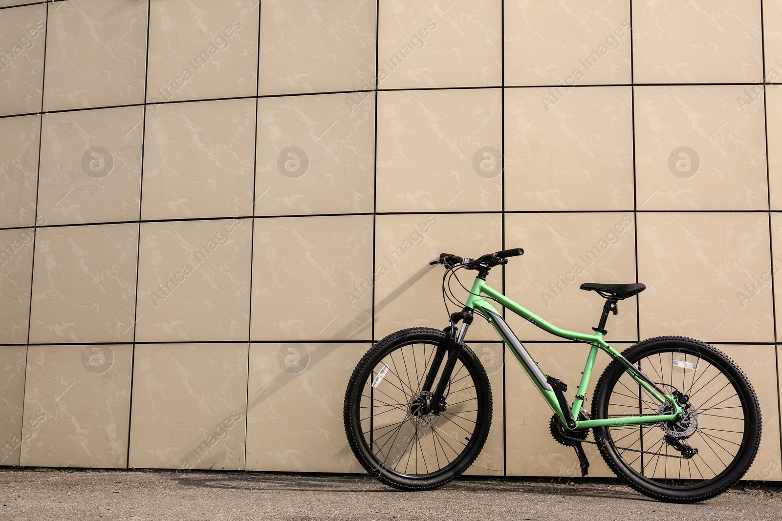 Photo of Modern bicycle near beige wall outdoors. Space for text