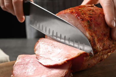 Photo of Woman cutting ham on wooden board at table, closeup