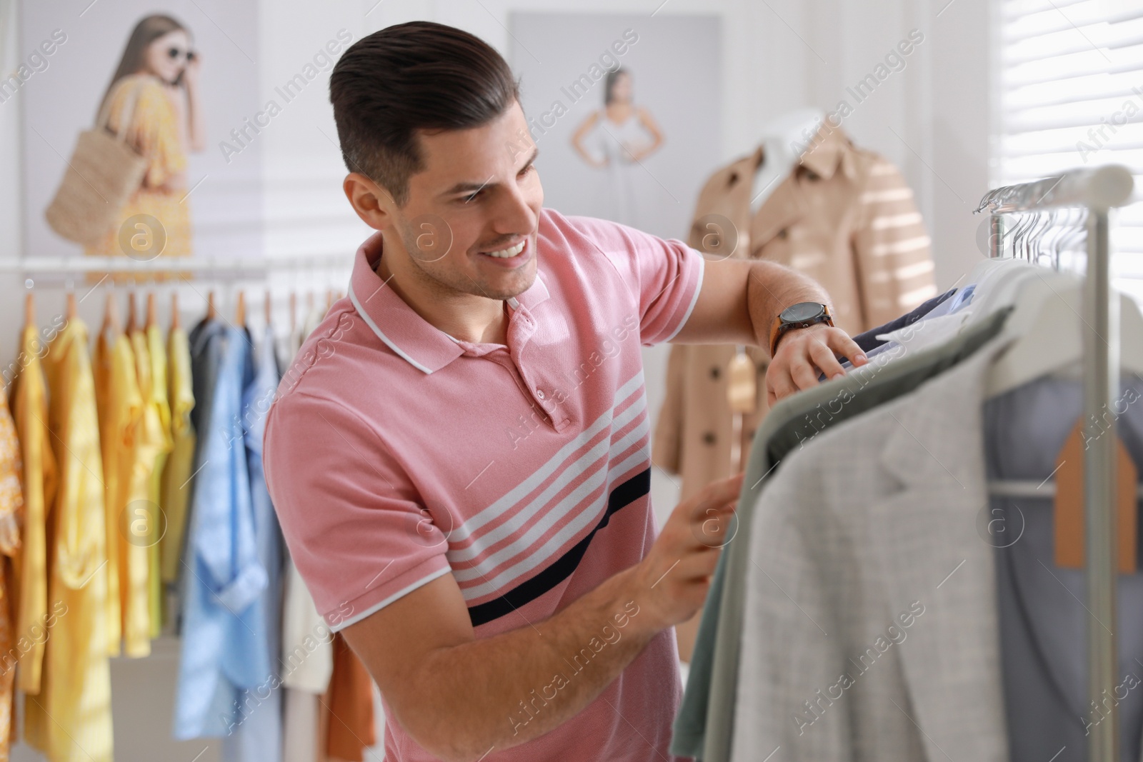 Photo of Man choosing clothes near rack in modern boutique