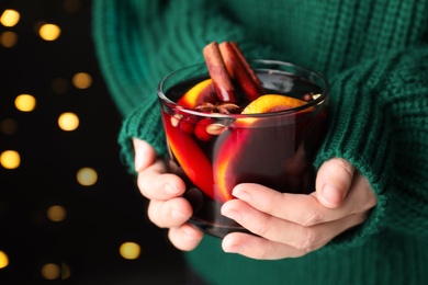 Photo of Woman holding cup of mulled wine against blurred lights, closeup