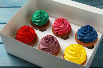 Photo of Box with different cupcakes on light blue wooden table, closeup
