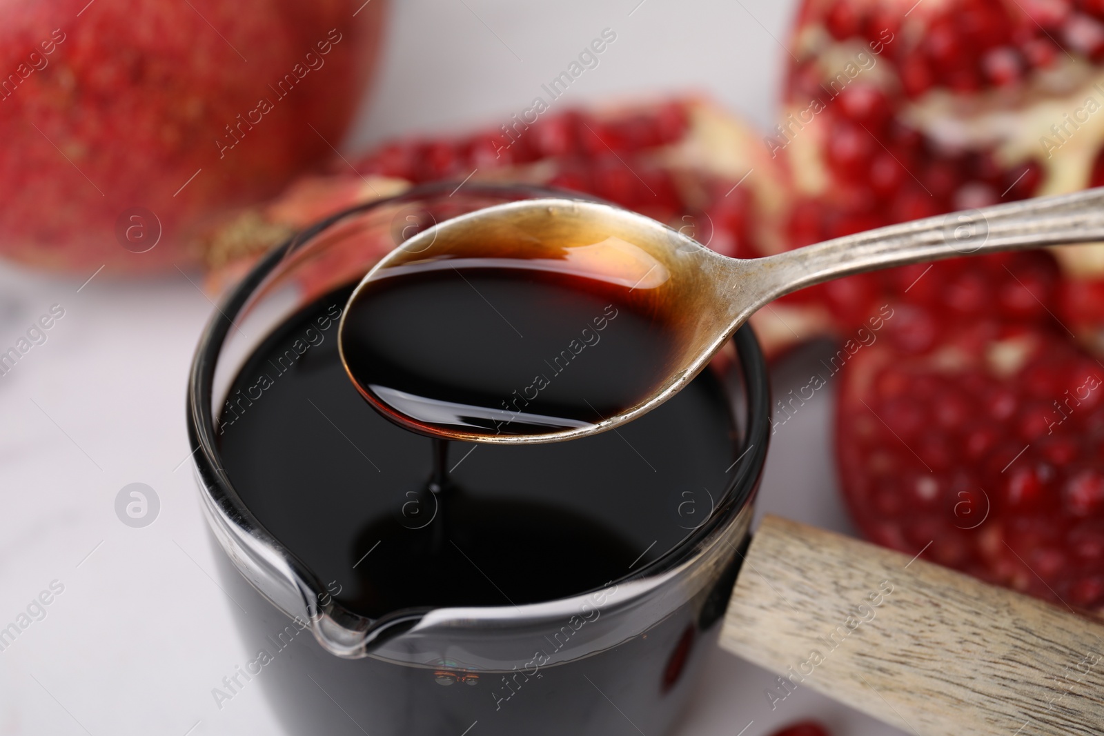 Photo of Taking tasty pomegranate sauce with spoon at white table, closeup