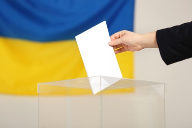 Photo of Woman putting voting paper into ballot box against Ukrainian flag, closeup