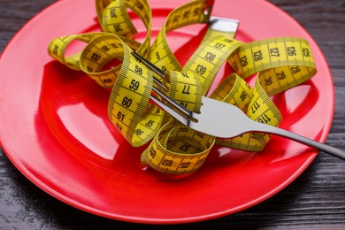 Photo of Plate with measuring tape and fork on wooden table, closeup. Weight loss concept