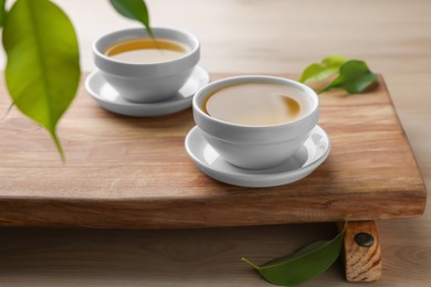 Photo of Tray with white cups of green tea and leaves on wooden table
