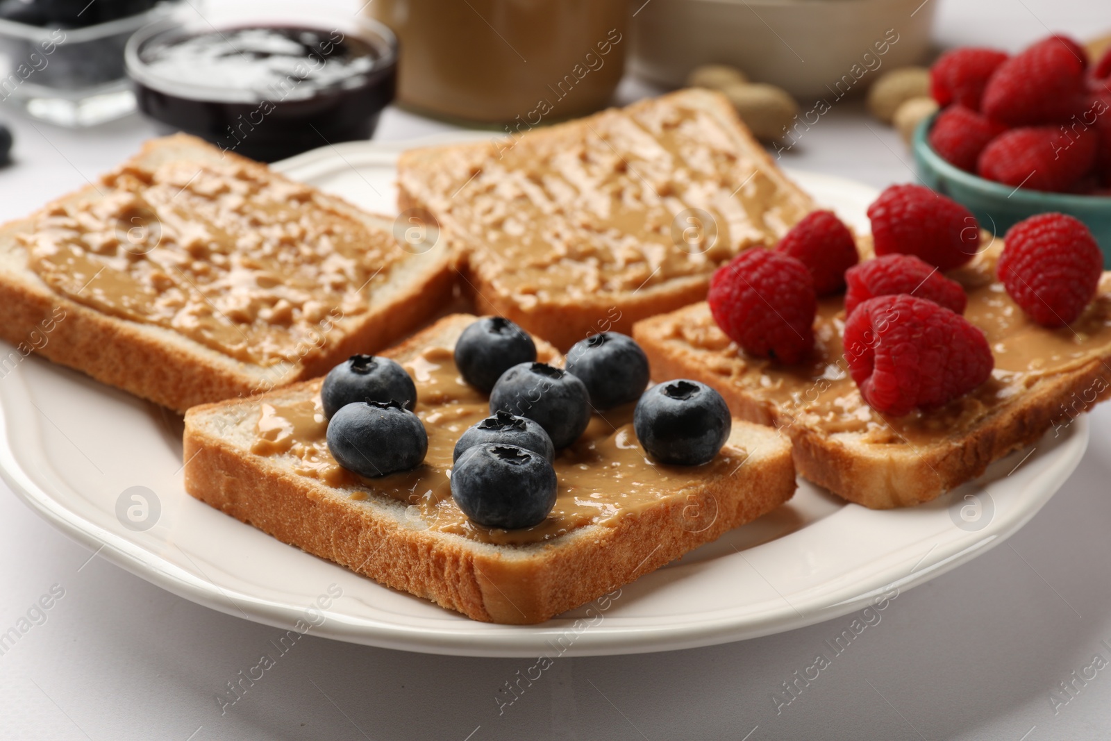 Photo of Delicious toasts with peanut butter, raspberries and blueberries on white table, closeup