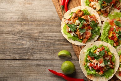 Delicious tacos with vegetables, meat and lime on wooden table, flat lay. Space for text