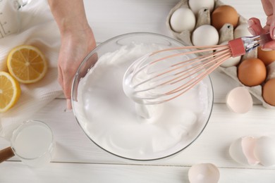 Photo of Woman making whipped cream with whisk at white wooden table, above view