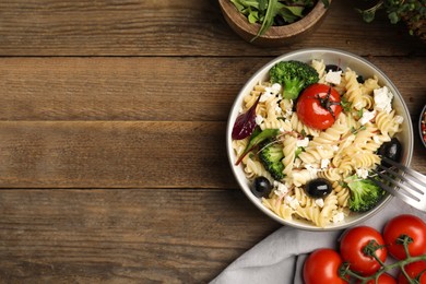 Photo of Bowl of delicious pasta with tomatoes, olives and broccoli on wooden table, flat lay. Space for text