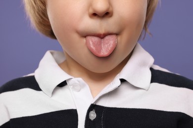 Photo of Little boy showing his tongue on purple background, closeup