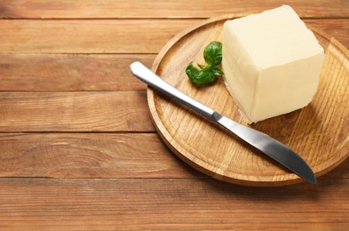 Photo of Block of tasty butter, knife and basil on wooden table. Space for text