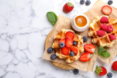 Photo of Delicious Belgian waffles with fresh berries and honey on white marble table, flat lay. Space for text