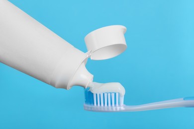 Photo of Applying paste on toothbrush against light blue background, closeup