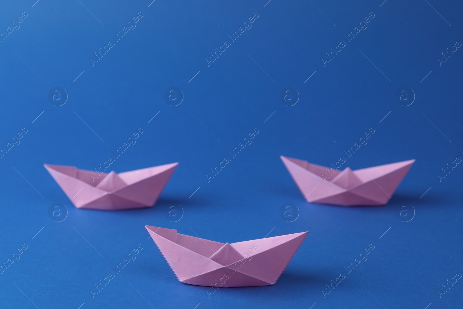 Photo of Handmade violet paper boats on blue background. Origami art