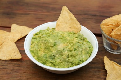 Photo of Delicious guacamole made of avocados with nachos on wooden table, closeup